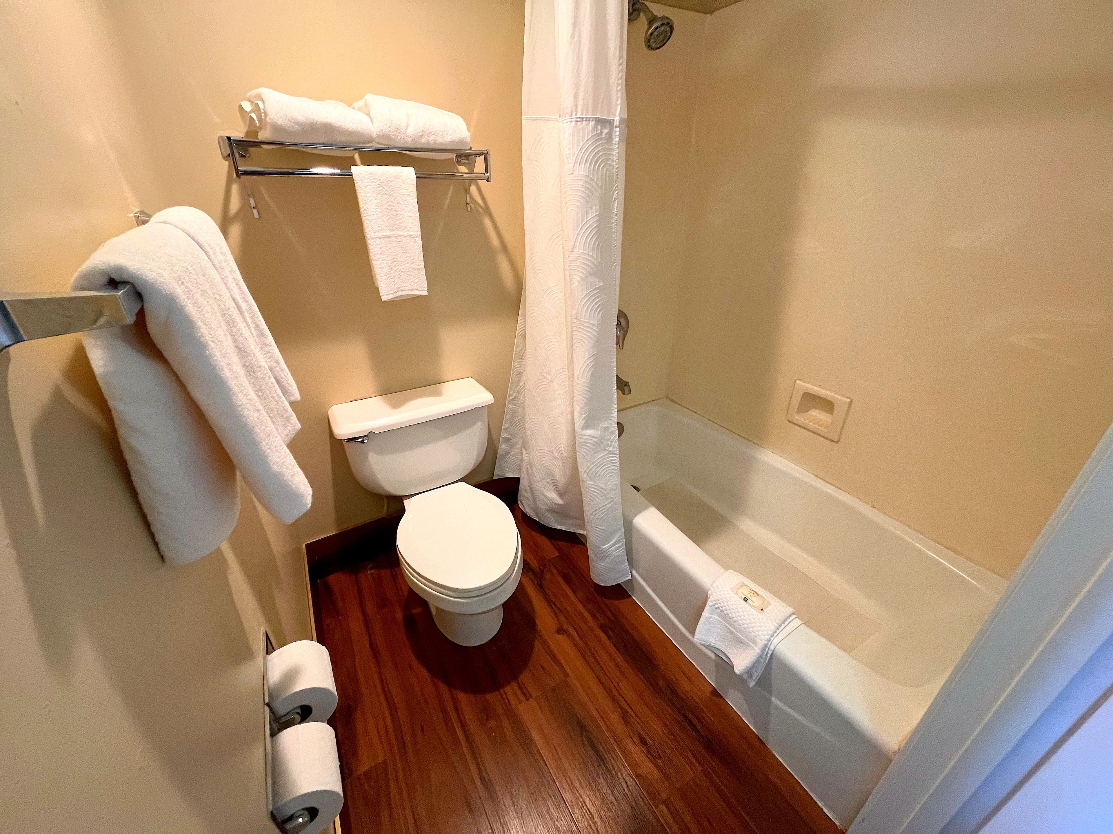 A bathroom with a toilet, a shower with a curtain, and a towel rack with towels.