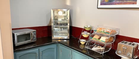 A kitchenette with a microwave, a refrigerator, a toaster, and a bread display.