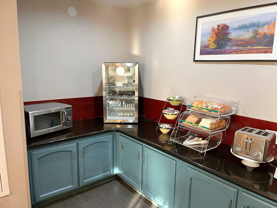Een kitchenette met een magnetron, een koelkast, een broodrooster en een broodvitrine.