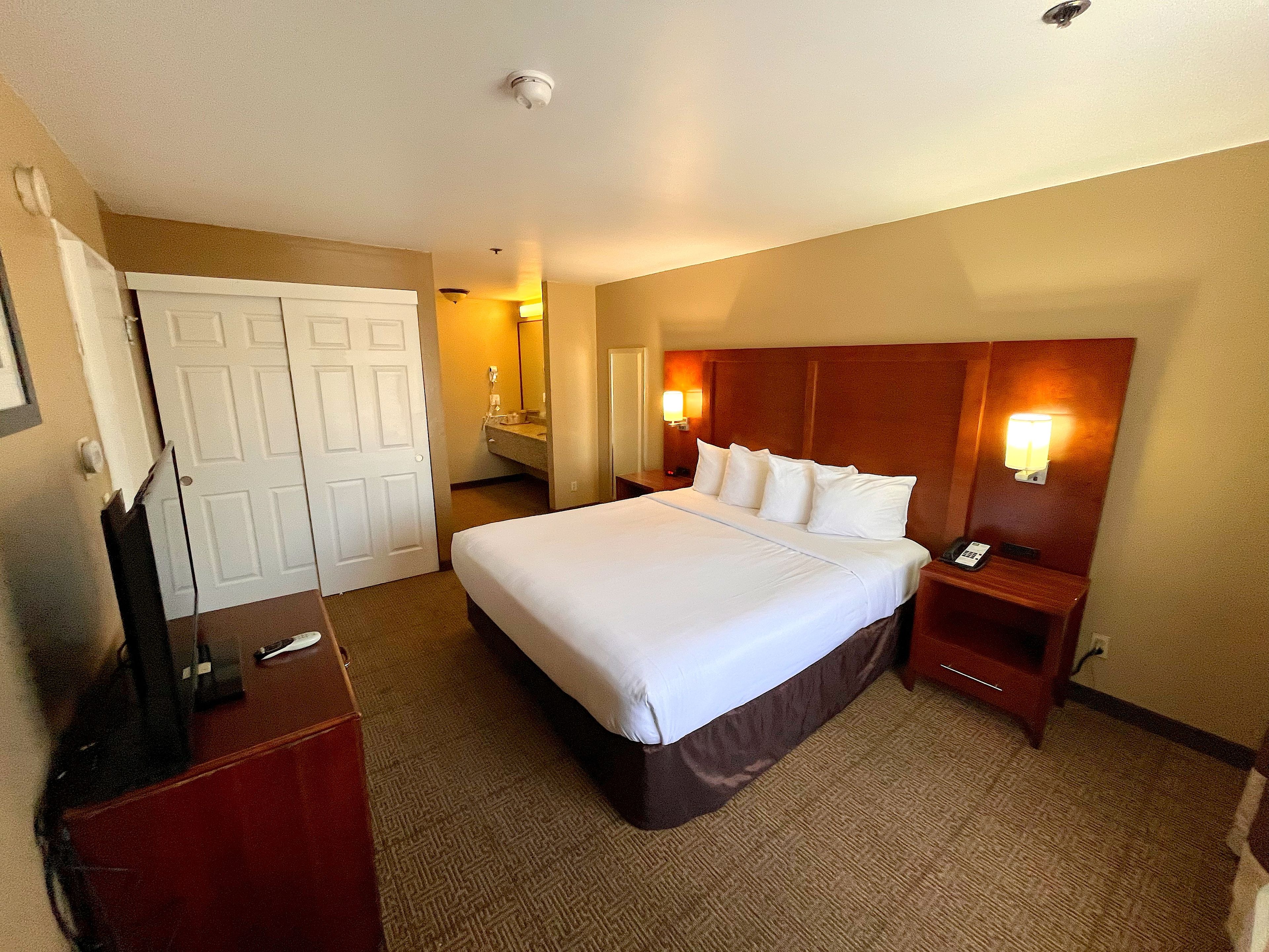 A hotel room with a large bed, a desk, a wardrobe, and a bathroom visible through an open door.