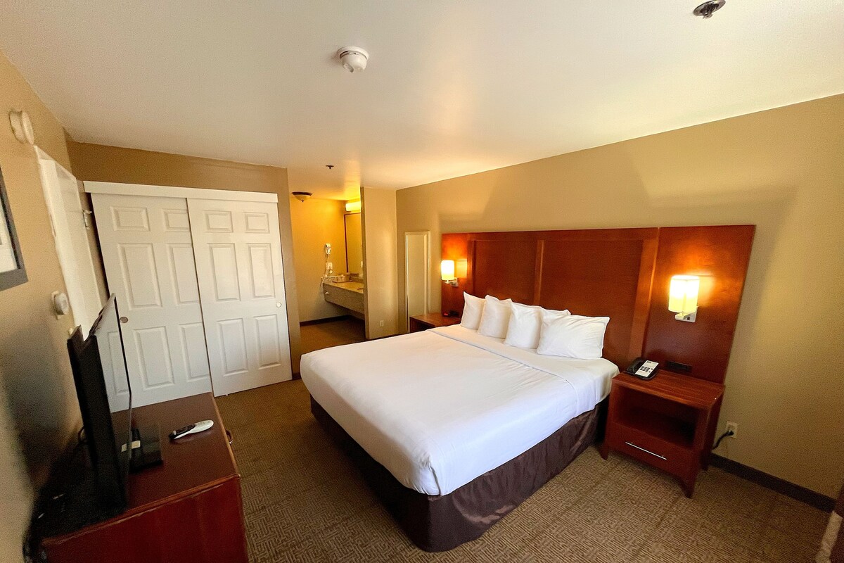 A hotel room with a large bed, a desk, a wardrobe, and a bathroom visible through an open door.