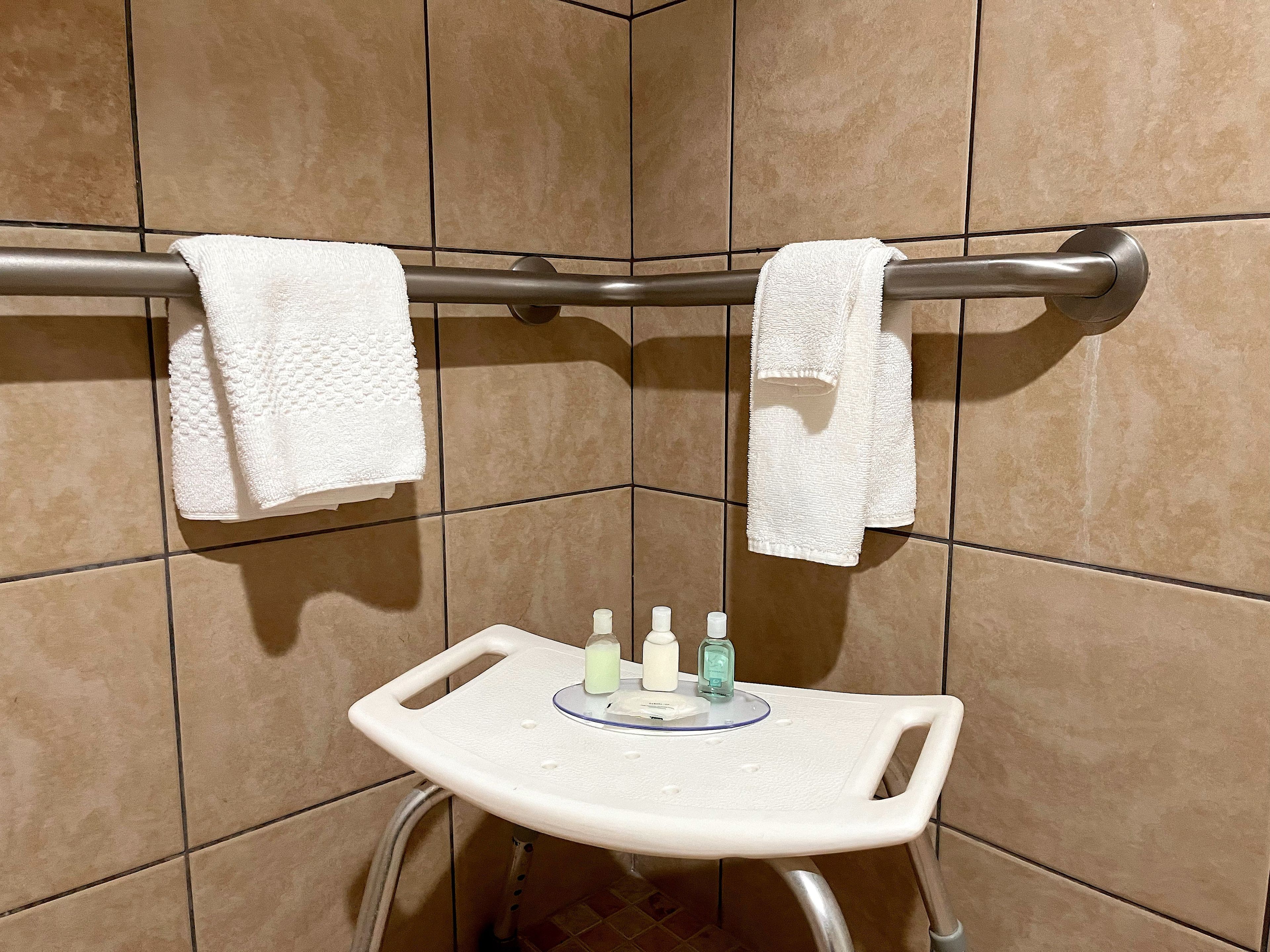 A shower area with a grab bar, two white towels, and a small table with toiletries.