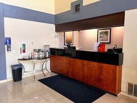Zona de recepción de hotel con mostrador de madera, quiosco de registro, dispensador de gel antibacterial y un basurero.