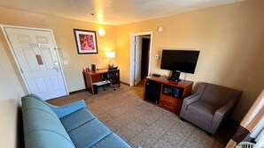 A hotel room with a sofa, a chair, a desk with a computer, a TV, and a microwave.