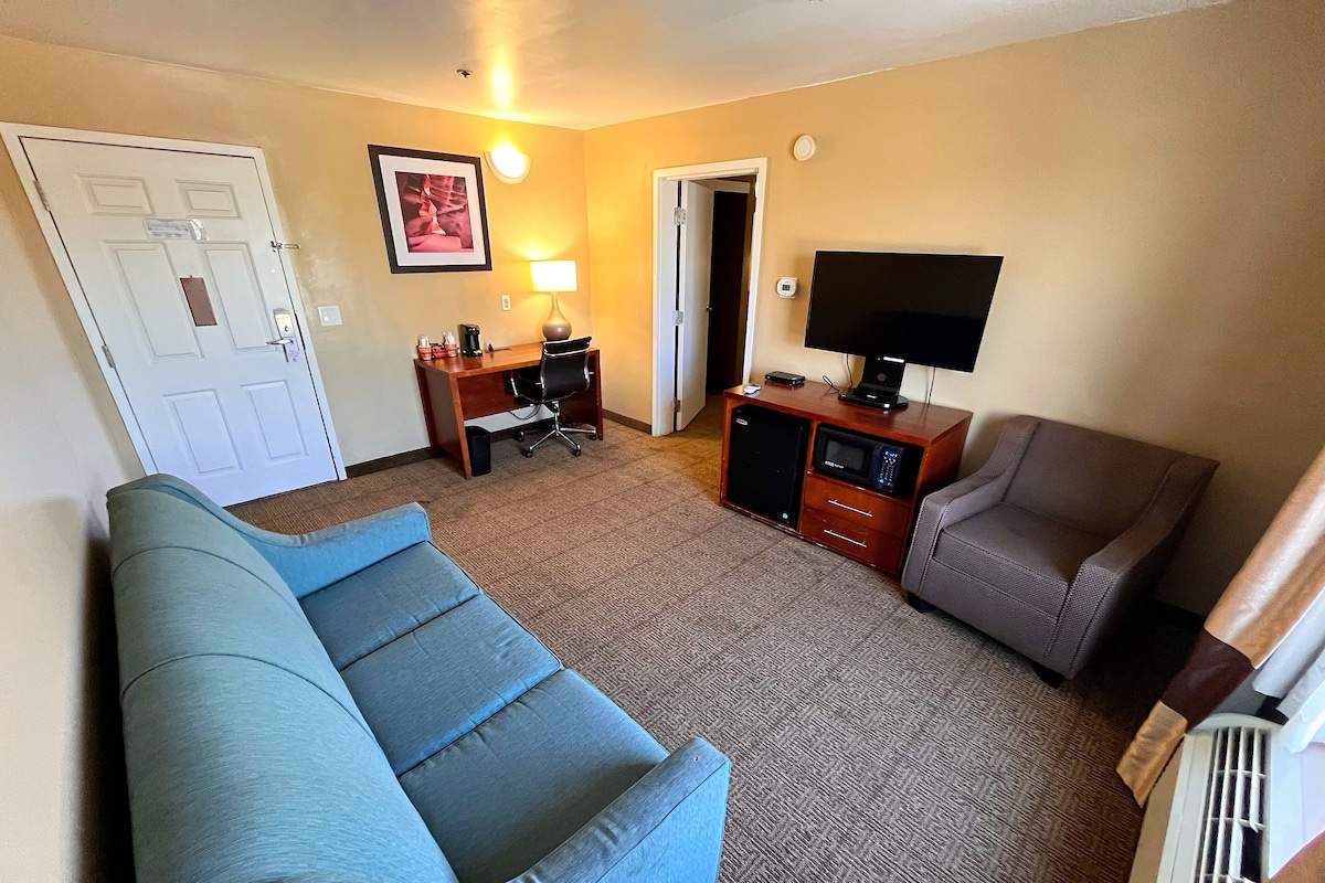 A hotel room with a sofa, a chair, a desk with a computer, a TV, and a microwave.