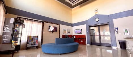 A hotel lobby with a vending machine, a television, a blue seating area, and a reception desk.
