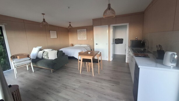 Una habitación compacta con cama, sofá, mesa de comedor y kitchenette.