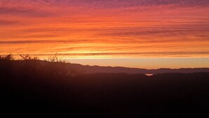 Atardecer sobre un paisaje montañoso con siluetas de vegetación y colinas distantes.