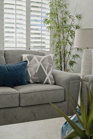 Ein graues Sofa mit gemusterten Kissen, eine hohe Bambuspflanze und eine weiße Lampe.