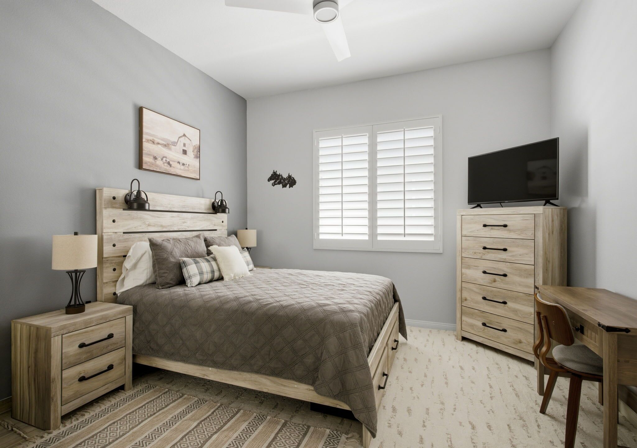 A bedroom with a bed, bedside tables, a desk, a chair, a television, and a window with blinds.