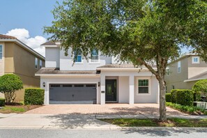 A two-story residential building with a garage, a front door, and a small porch area. - Encore 10BR Escape with Pool, Spa & Game Room (Kissimmee)