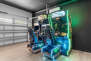 A row of arcade racing game machines with 'The Fast and the Furious' branding, positioned in a room with a garage door and wooden flooring. - Encore 10BR Escape with Pool, Spa & Game Room (Kissimmee)