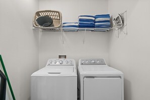 A laundry room with two front-loading washing machines, a drying rack with folded towels, and a basket. - Encore 10BR Escape with Pool, Spa & Game Room (Kissimmee)
