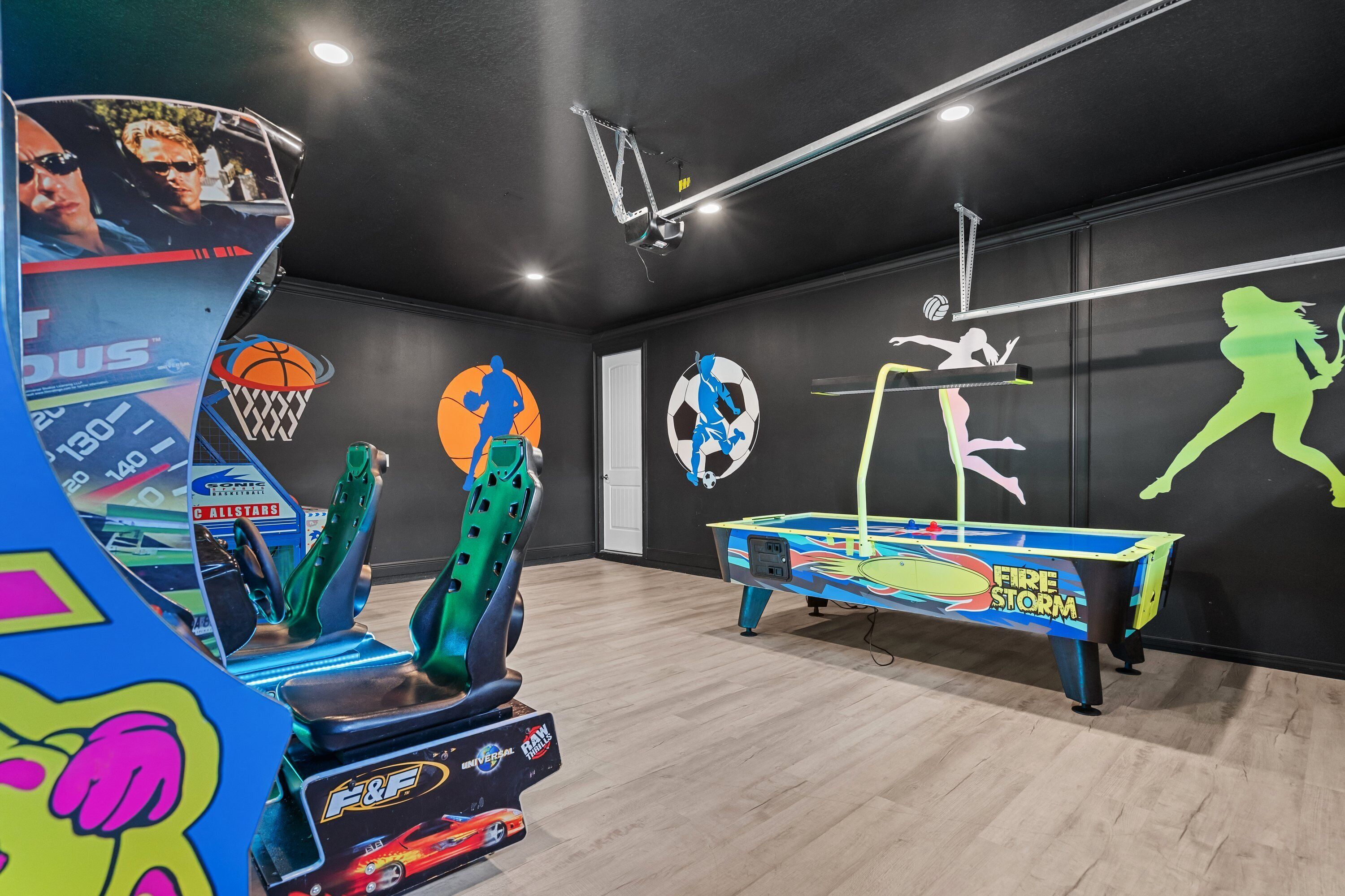 Une pièce équipée d’une table de billard, de jeux d’arcade et décorée de motifs muraux sur le thème du sport.