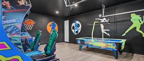 Une pièce équipée d’une table de billard, de jeux d’arcade et décorée de motifs muraux sur le thème du sport.