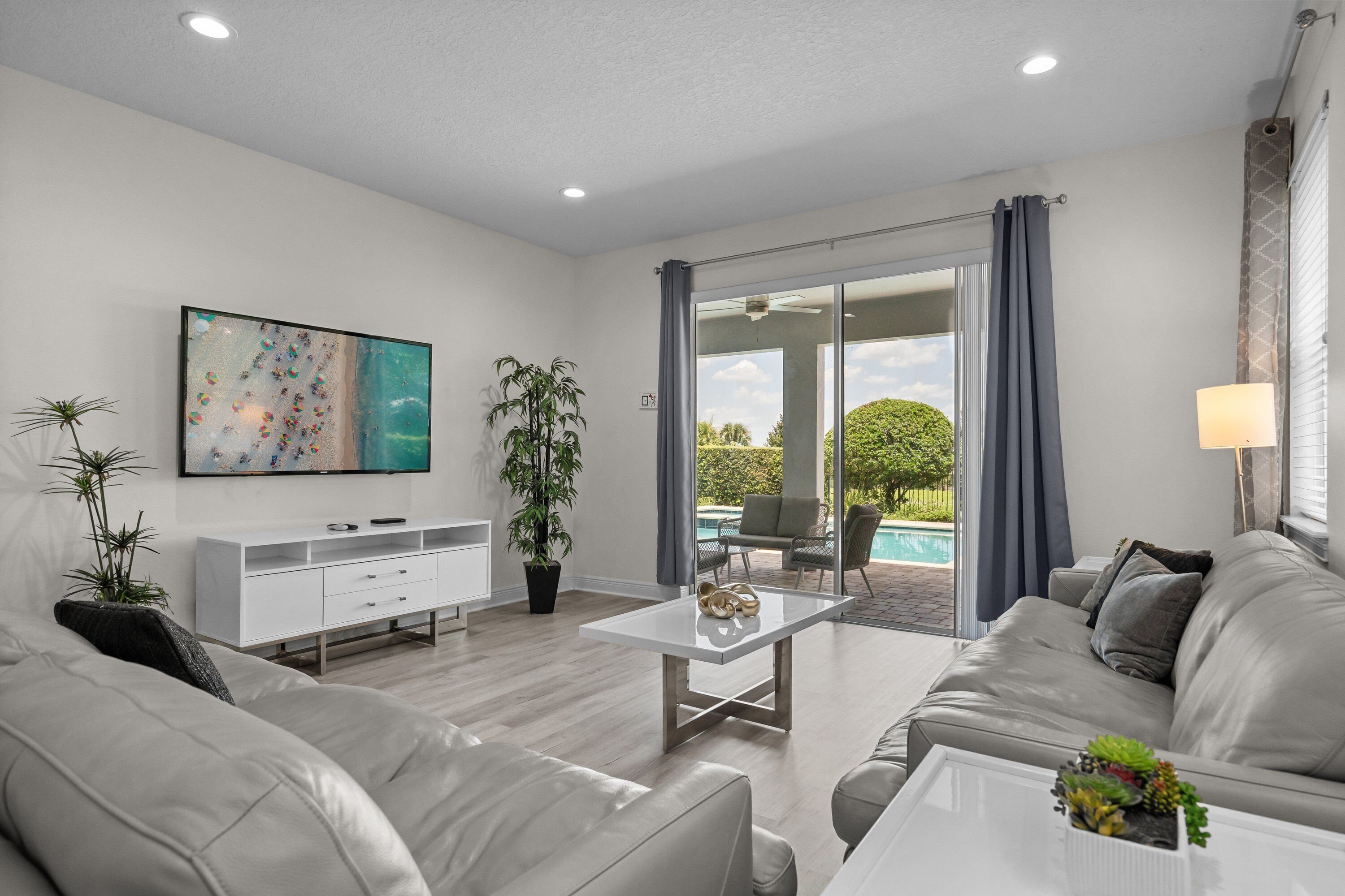 A modern living room with a sofa, coffee table, TV, and a view of a pool.