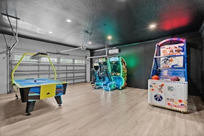 A room with a ping pong table, two arcade machines, and a basketball-themed vending machine. - Encore 10BR Escape with Pool, Spa & Game Room (Kissimmee)