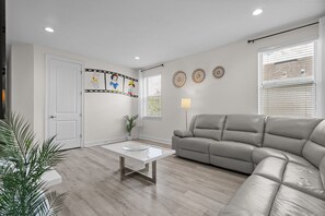 A modern living room with a grey sofa, a glass coffee table, and a door with a film strip mural. - Encore 10BR Escape with Pool, Spa & Game Room (Kissimmee)