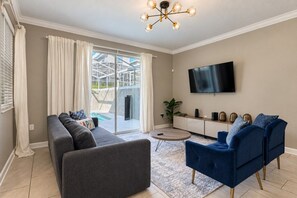 Un salon avec un canapé, un fauteuil bleu, un téléviseur à écran plat et un lustre.
