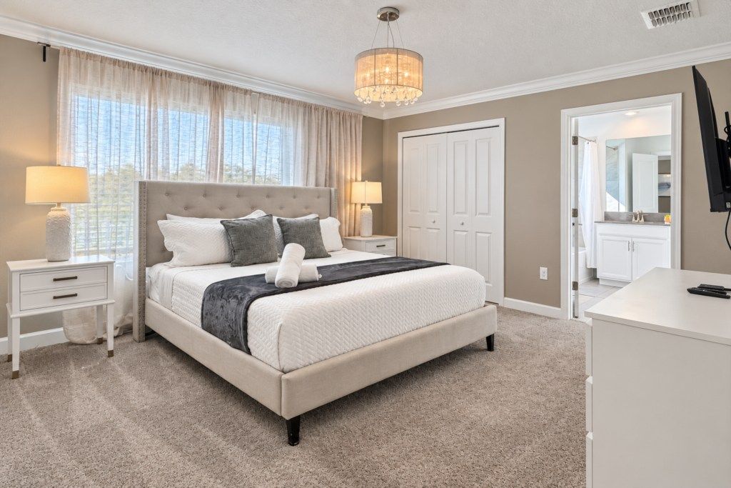 A bedroom with a large bed, two bedside tables, a chandelier, a wardrobe, and a desk.