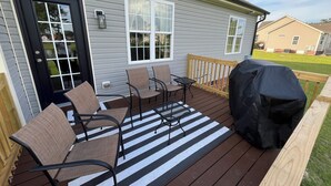 Eine Terrasse mit Gartenmöbeln, einem Grill und einem Haus mit grauer Außenfassade.