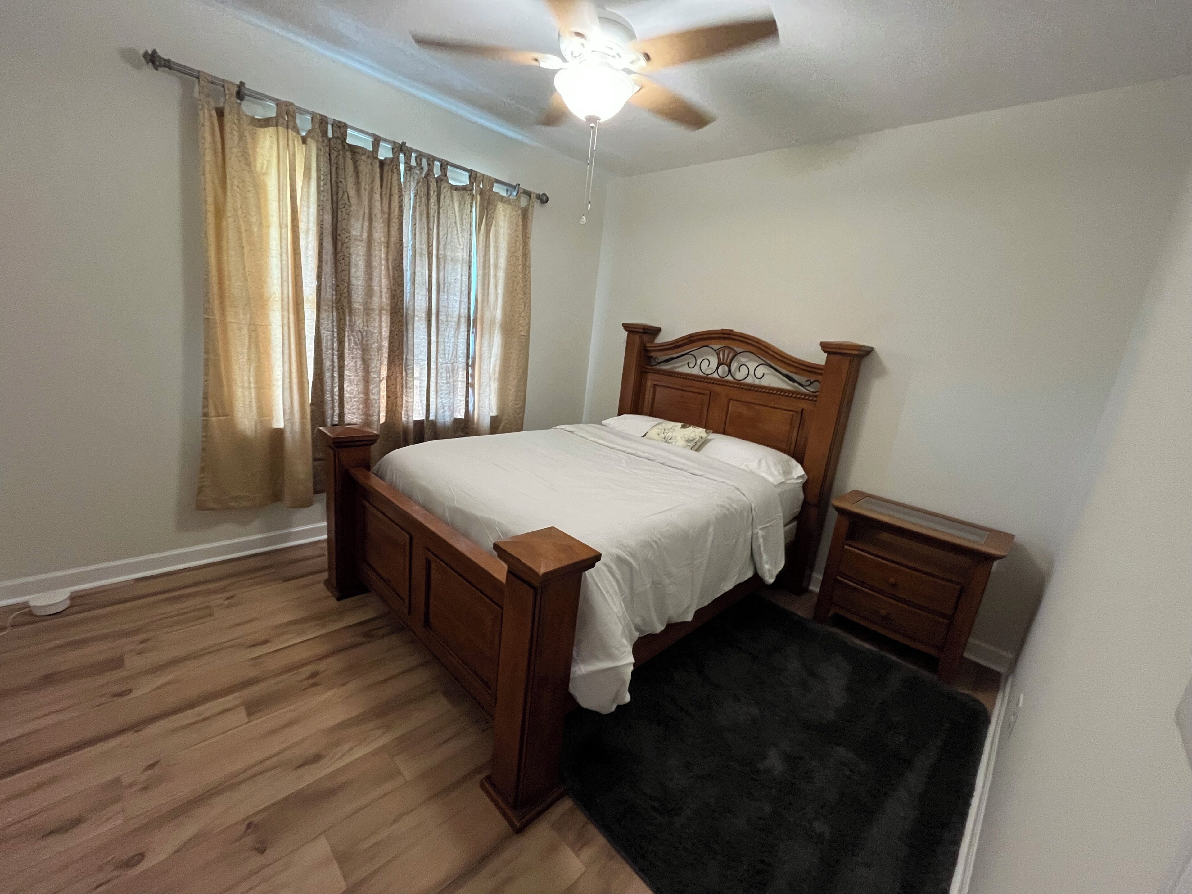Un dormitorio con una cama de madera, una mesita de noche y cortinas en la ventana.
