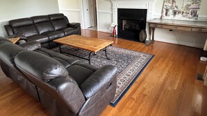 Ein Wohnzimmer mit einem ledernen Ecksofa, einem Holztisch, einem Kamin und einem flachbildfernseher, der darüber angebracht ist.