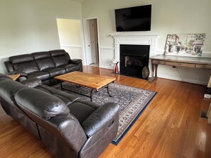 Ein Wohnzimmer mit einem ledernen Ecksofa, einem Holztisch, einem Kamin und einem flachbildfernseher, der darüber angebracht ist.