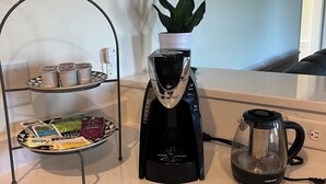 Eine Küchenarbeitsplatte mit Kaffeemaschine, einem Glas-Wasserkocher und einem Metallständer mit Teebeuteln und einer Topfpflanze.