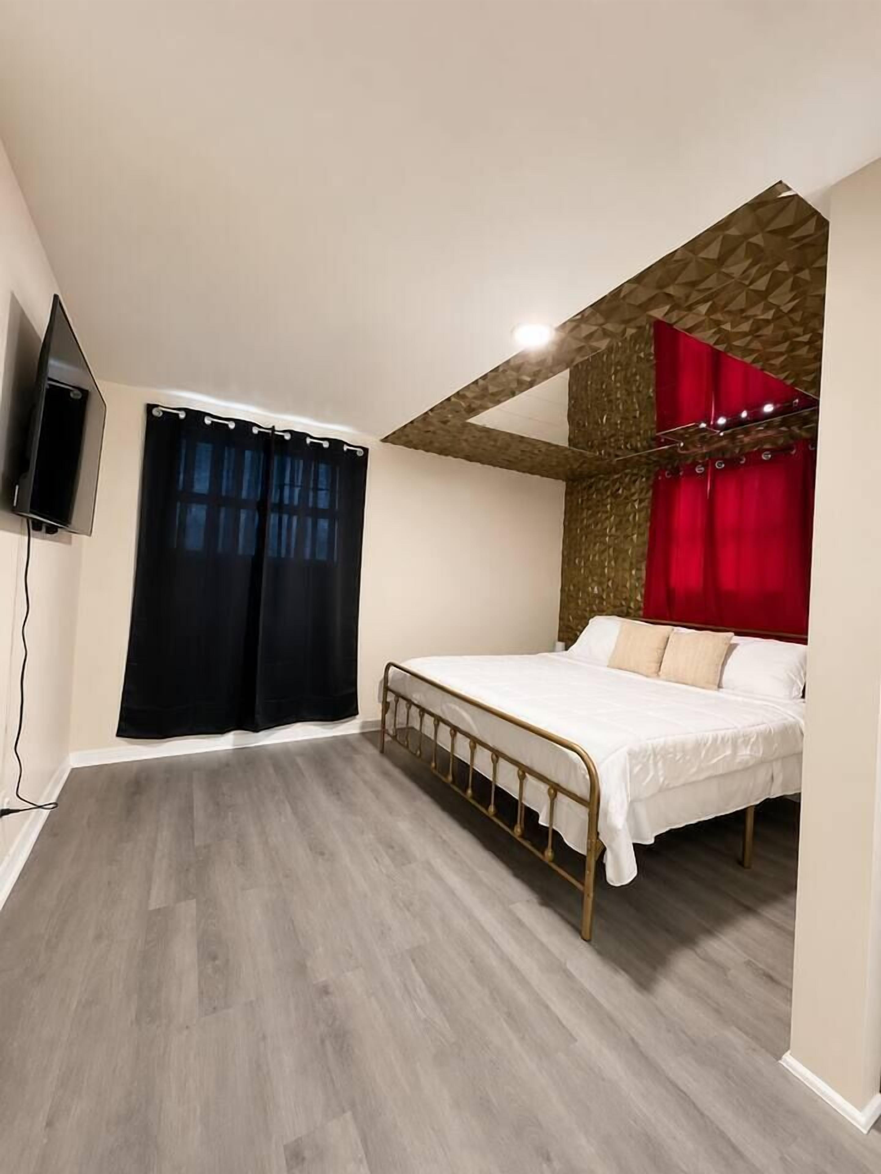 Ein Schlafzimmer mit Bett, Vorhängen, einem Fernseher und einer Holzbalkendecke.