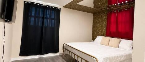 Un dormitorio con cama, cortinas, televisor y techo de madera.