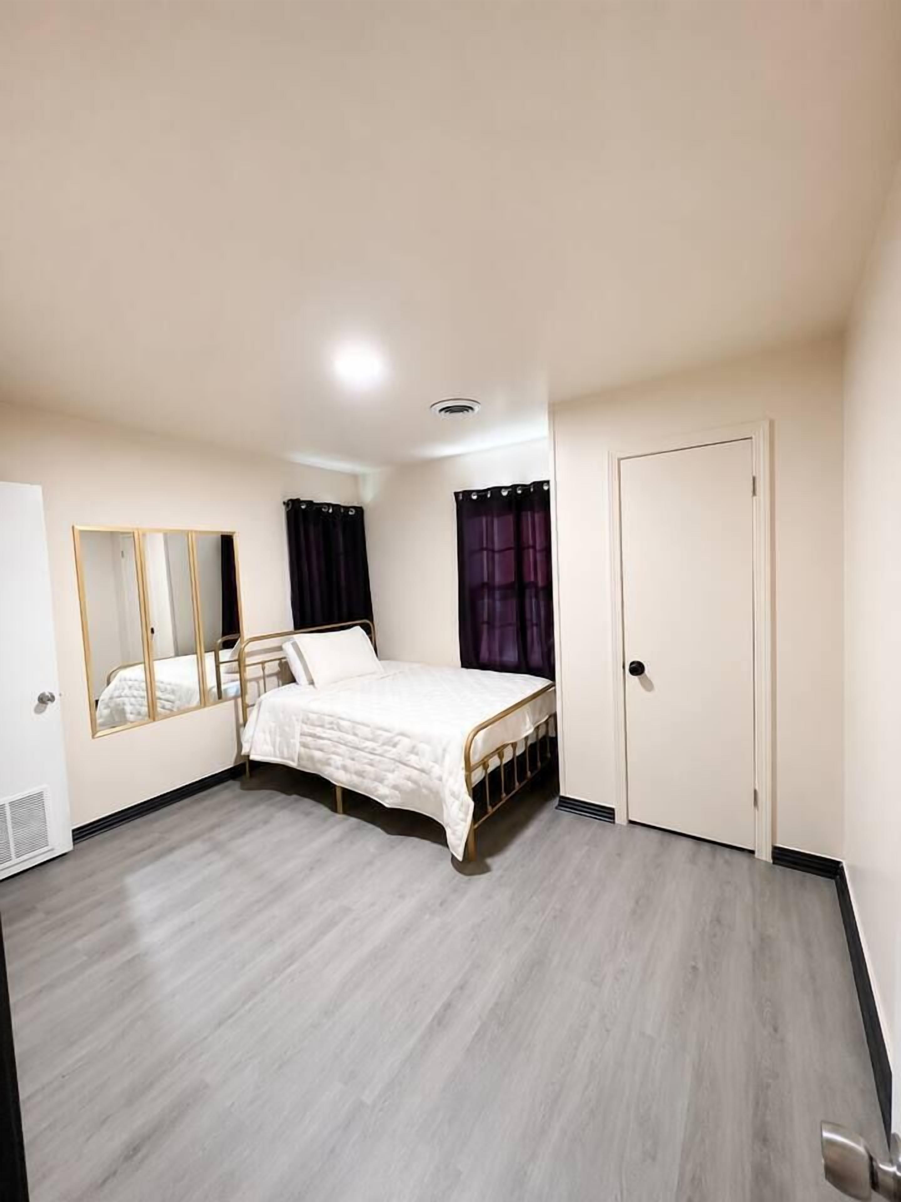 Un dormitorio con una cama, un espejo, una puerta y una ventana con cortinas.
