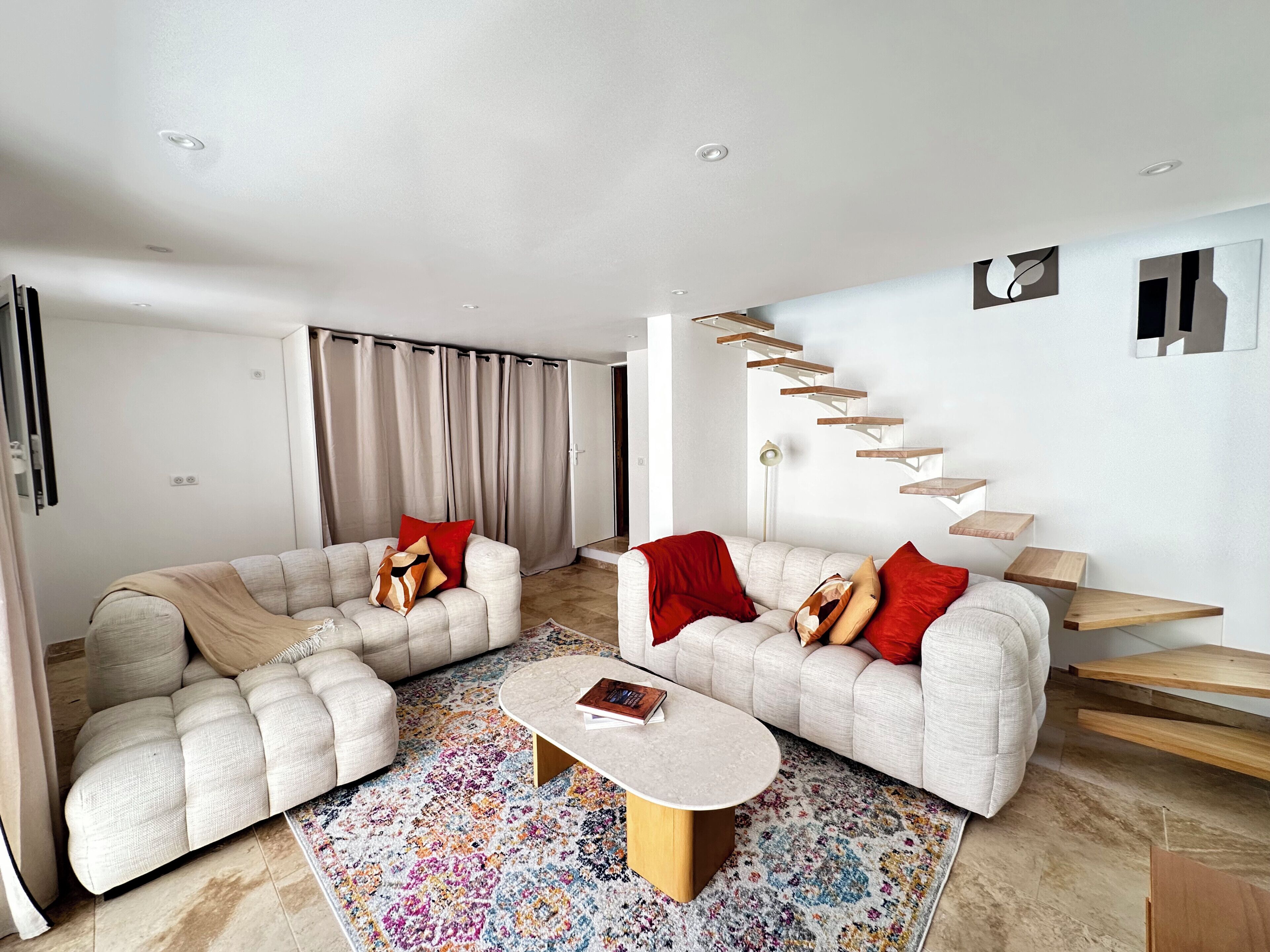 A modern living room with two sofas, a coffee table, a colorful rug, and a staircase with wooden shelves.