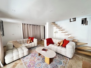 Ein modernes Wohnzimmer mit zwei Sofas, einem Couchtisch, einem farbenfrohen Teppich und einer Treppe mit Holzböden.