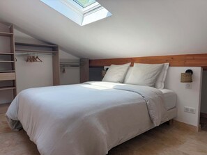 Une chambre dotée d’une lucarne, d’un lit avec une literie blanche, d’une tête de lit en bois et d’une armoire intégrée.