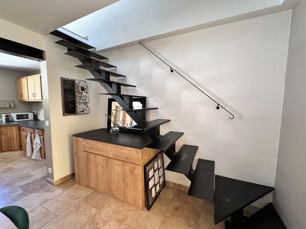 Une cuisine moderne avec un îlot central en bois, un escalier noir et une vue sur la salle à manger.