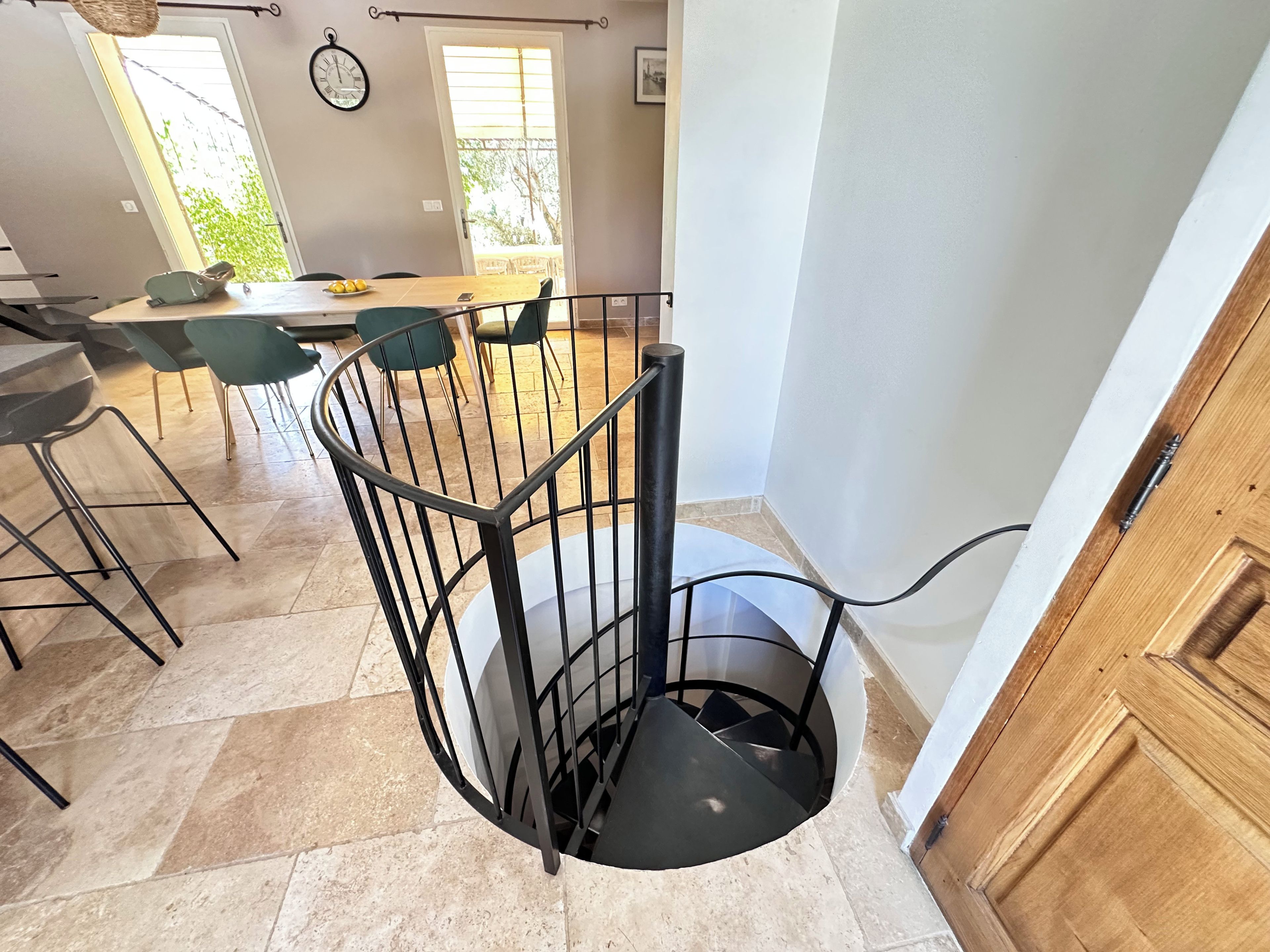 A spiral staircase with a metal railing leading to a dining area with chairs and a table.
