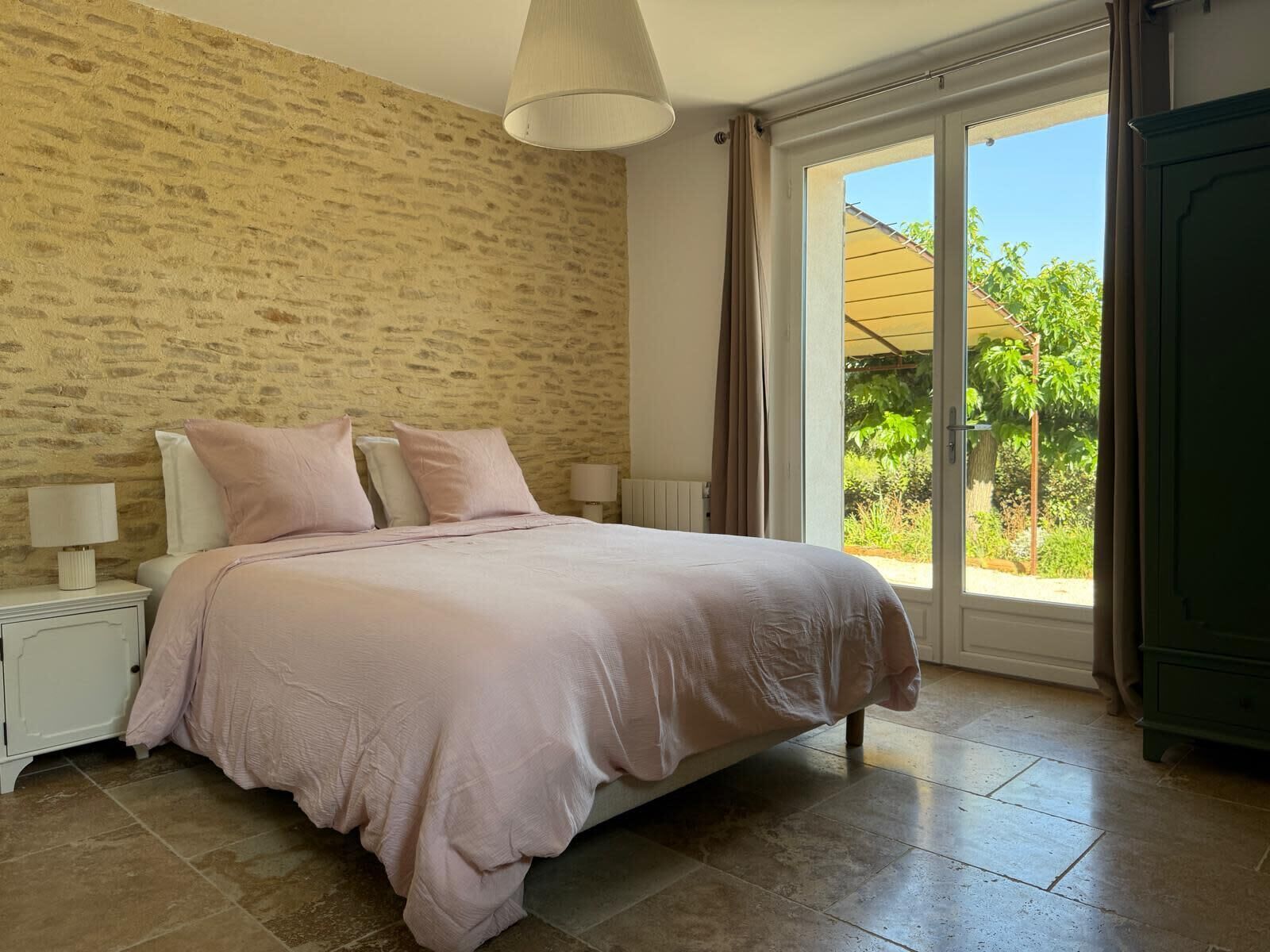 A bedroom with a bed, nightstands, a lamp, and a view of the outdoors.