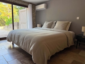 Ein Schlafzimmer mit einem großen Bett, einer Steinwand und Blick auf Bäume durch eine Schiebetür.
