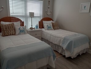 Ein Schlafzimmer mit zwei Betten, einem Nachttisch, einer Lampe und einem Fenster mit Jalousien.