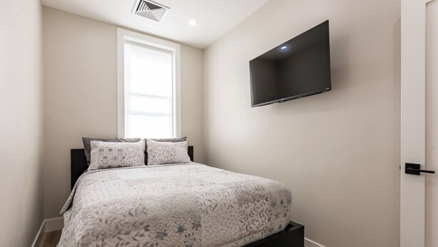 Een slaapkamer met een bed, een aan de muur bevestigde televisie en een raam.