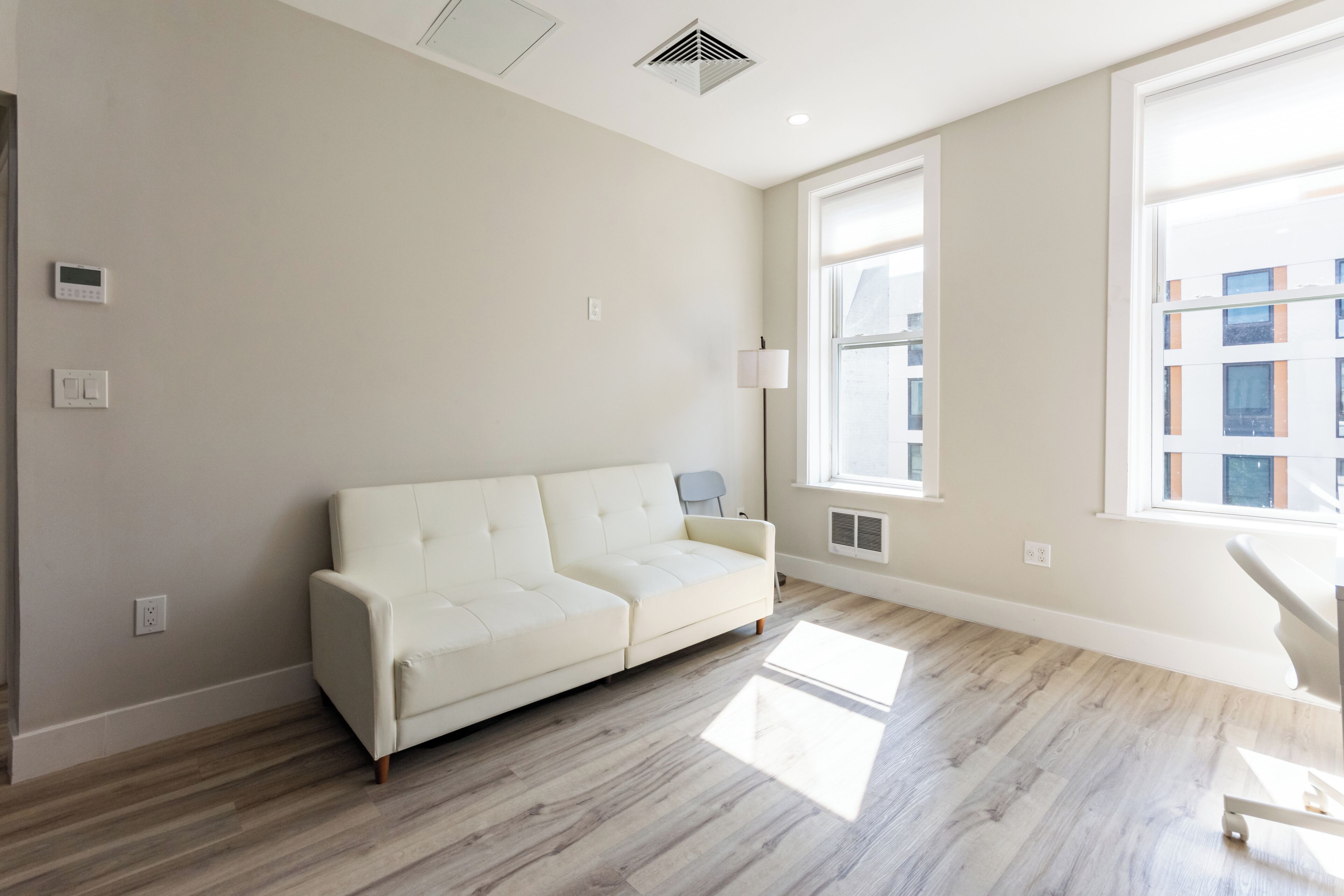 Een moderne woonkamer met een witte bank, grote ramen en een lichtgekleurde vloer.