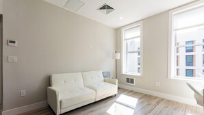 Een moderne woonkamer met een witte bank, grote ramen en een lichtgekleurde vloer.