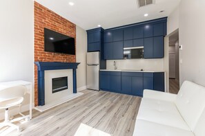 A modern kitchen with blue cabinets, a flat-screen TV, and a white sofa. - Stylish Brooklyn Apartment Natural Light (Brooklyn)