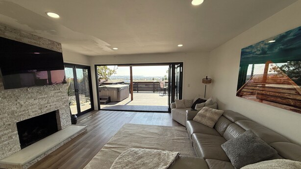 A modern living room with a fireplace, a large sofa, a flat-screen TV, and a view of the outdoors. - Pacific Beach Retreat Bay Views + Hot Tub (San Diego)