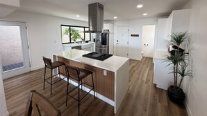 A modern kitchen with a central island, bar stools, a built-in oven, and a large window. - Pacific Beach Retreat Bay Views + Hot Tub (San Diego)