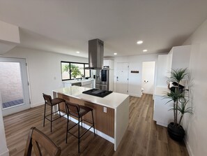 A modern kitchen with a central island, bar stools, a built-in oven, and a large window. - Pacific Beach Retreat Bay Views + Hot Tub (San Diego)