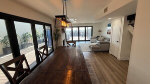 A spacious living area with a wooden dining table, a sofa, and a large window offering a view of the outdoors. - Pacific Beach Retreat Bay Views + Hot Tub (San Diego)