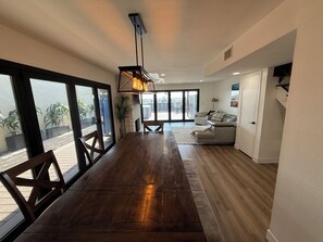 A spacious living area with a wooden dining table, a sofa, and a large window offering a view of the outdoors. - Pacific Beach Retreat Bay Views + Hot Tub (San Diego)