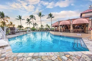 A swimming pool with a stone deck, palm trees, and a building with a red roof. - Spacious 3-bedroom condo in a peaceful location with AC and gym (Kailua-Kona)